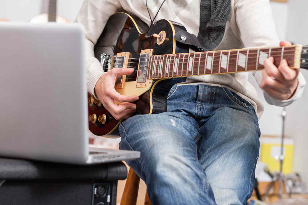 Man recording guitar playing in front of laptop